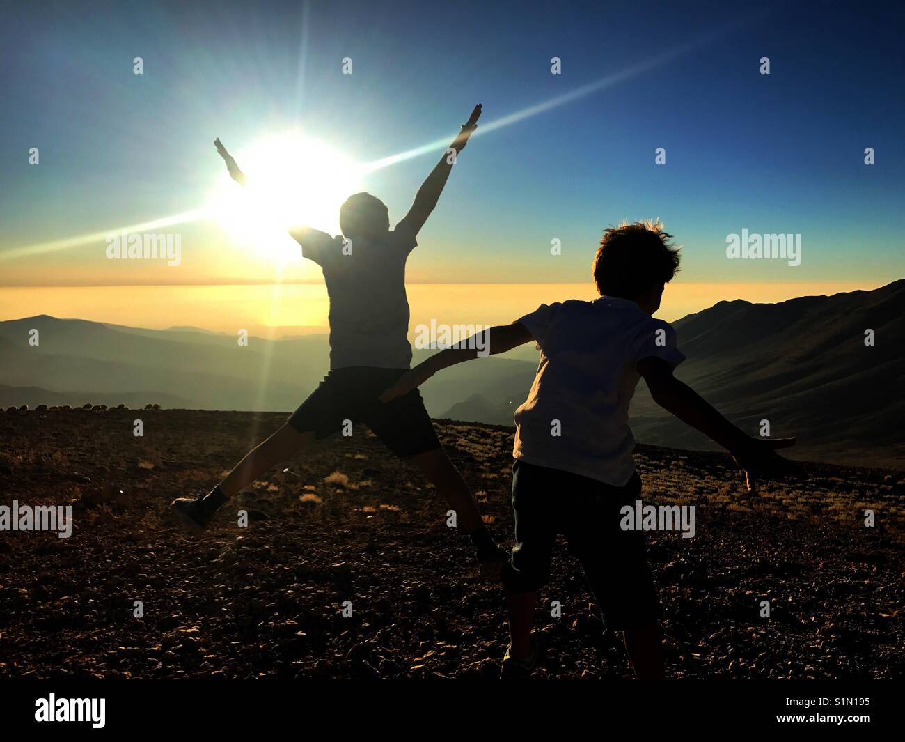 Two boys silhouette jumping happily on top of the cliff - Smartphone Captured Stock Image