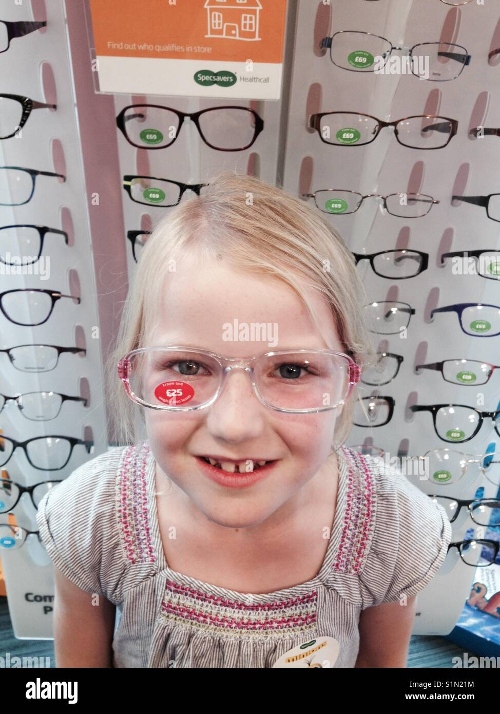 Seven year old girl tries new prescription glasses / spectacles on at an optician store. Stock Photo