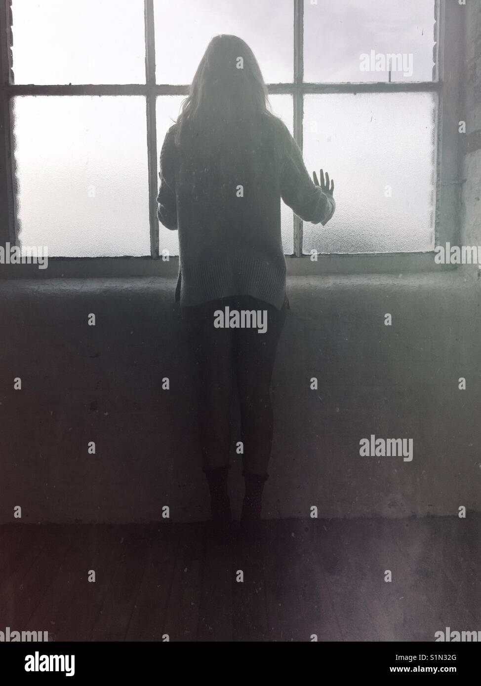 Rear view silhouette of a woman standing by the window Stock Photo
