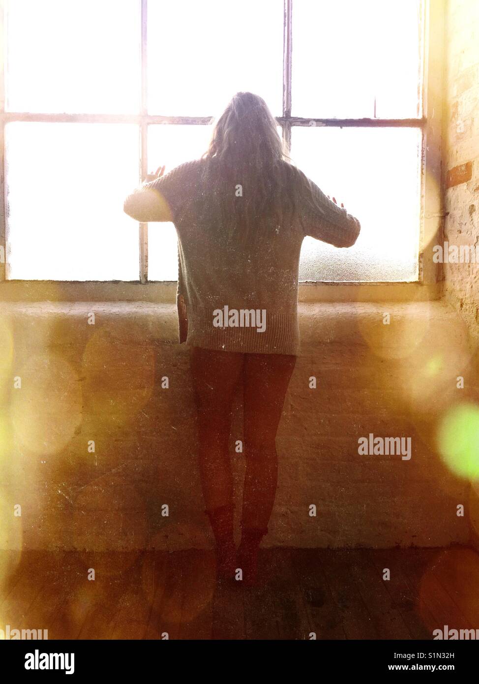 Rear view of a blond woman standing by he window - Smartphone Captured Stock Image