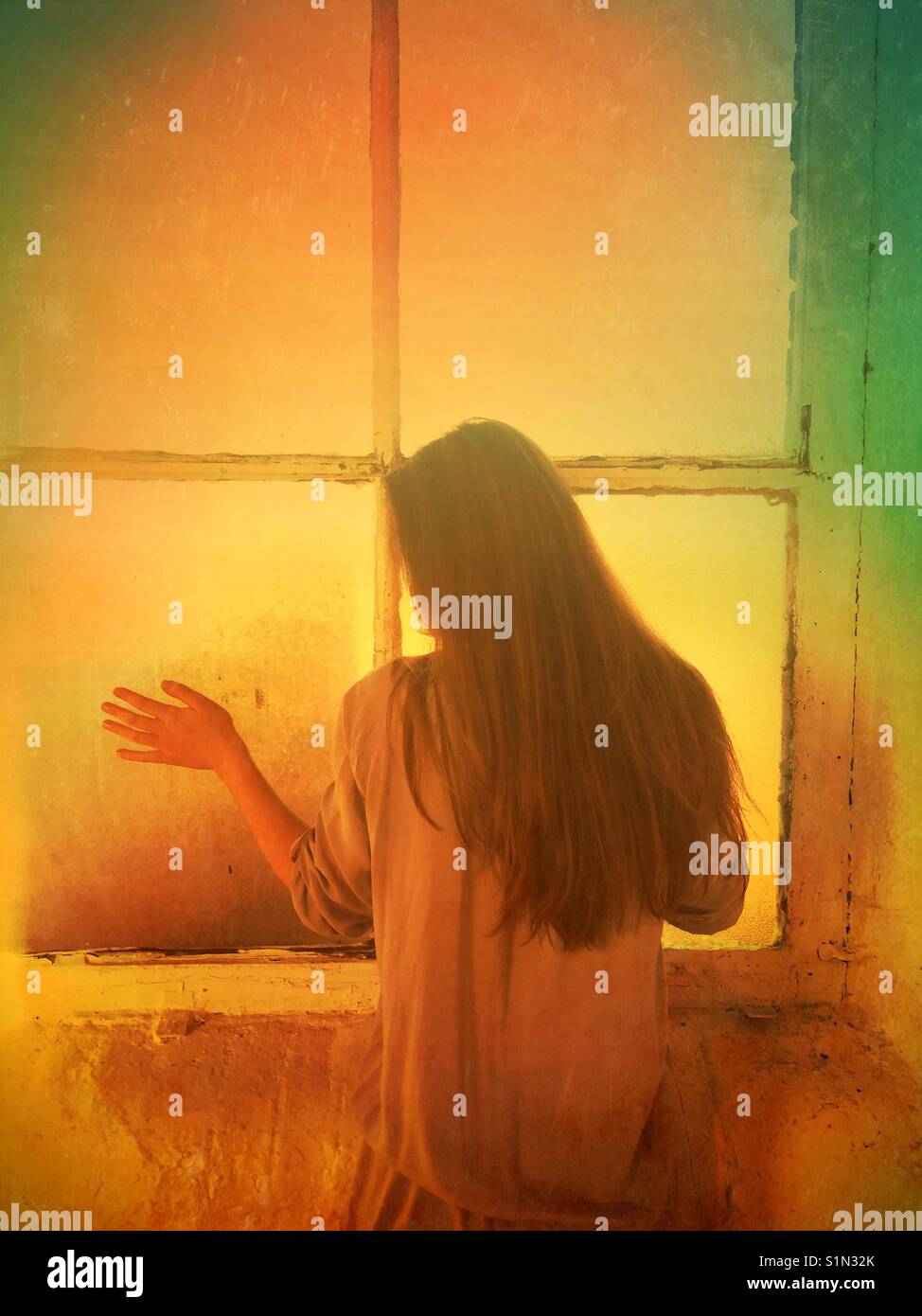 Rear view of a lonely woman standing by the window hand touching the glass - Smartphone Captured Stock Image