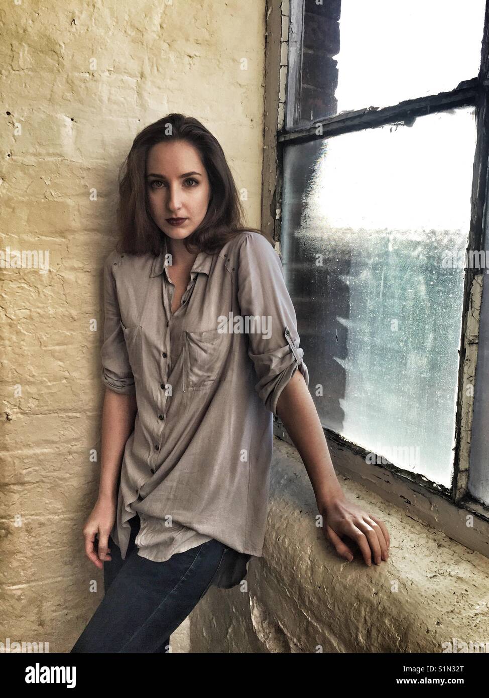 Scared beautiful young woman standing by the window - Smartphone Captured Stock Image