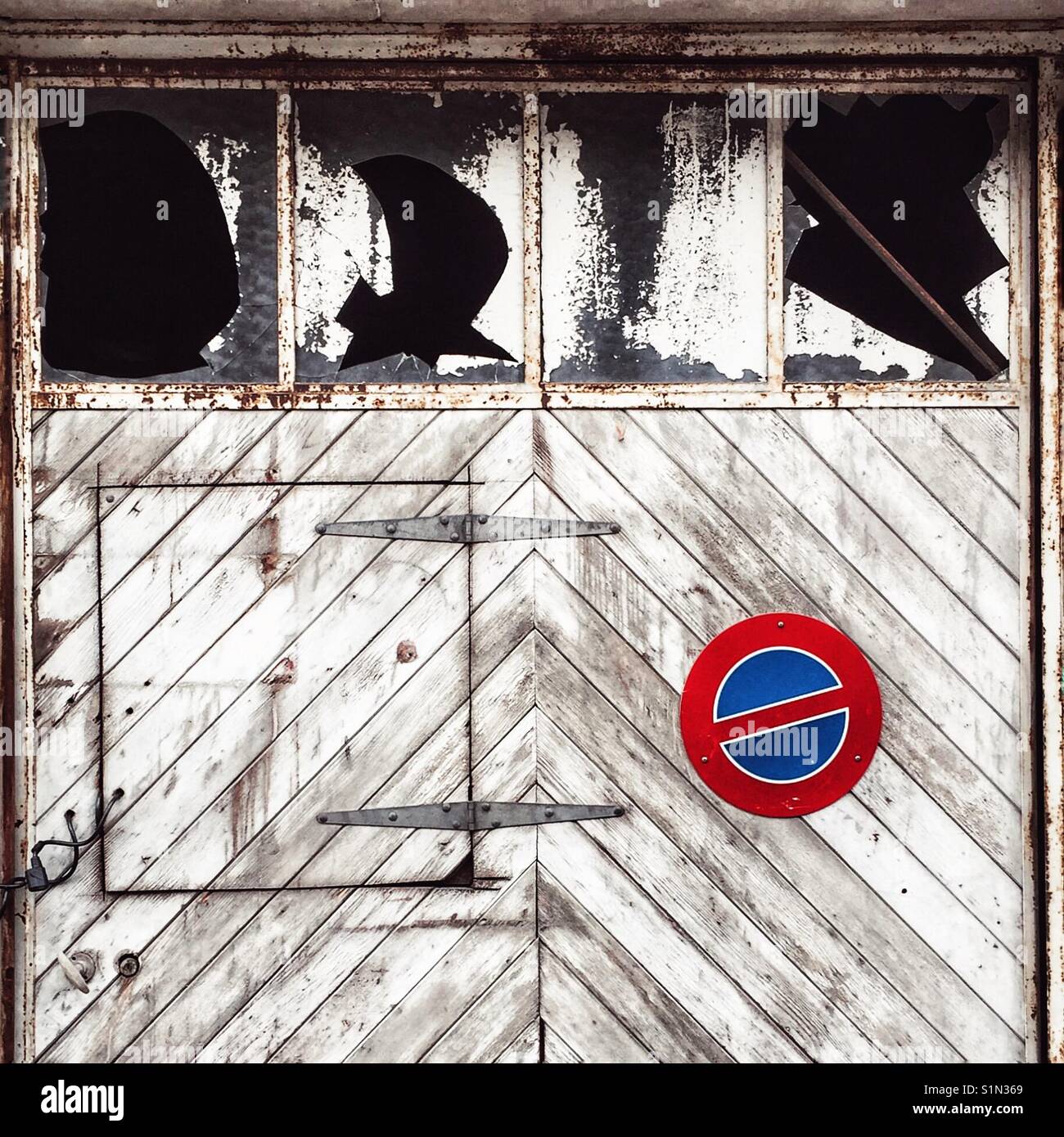 No parking sign on derelict garage doors with broken windows - Smartphone Captured Stock Image
