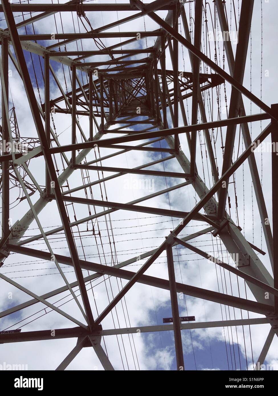 Looking up inside an electricity transmission tower from the ground on a cloudy day Stock Photo