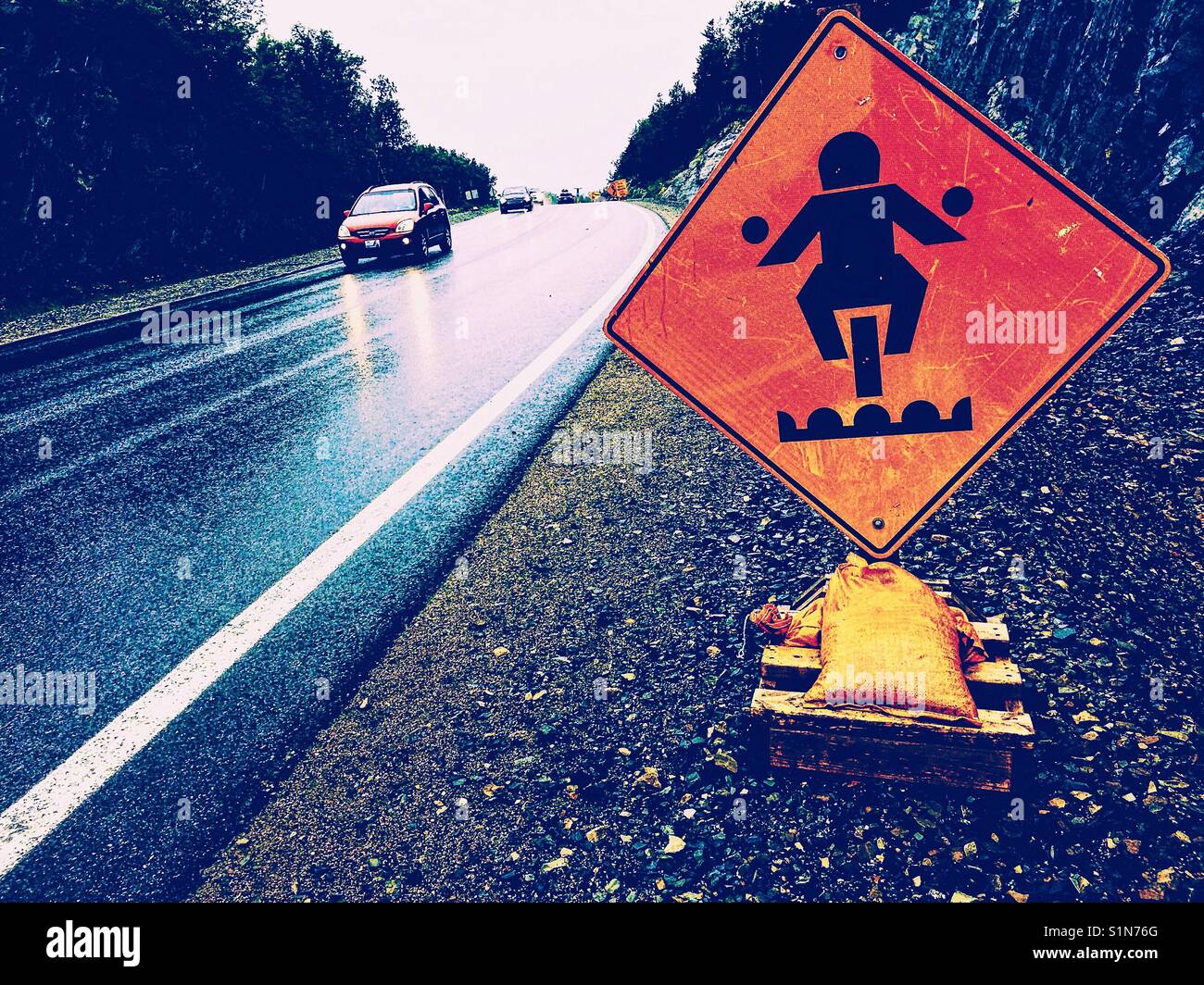 Bumpy road ahead warning sign for motorcyclists next to wet highway, Canada Stock Photo