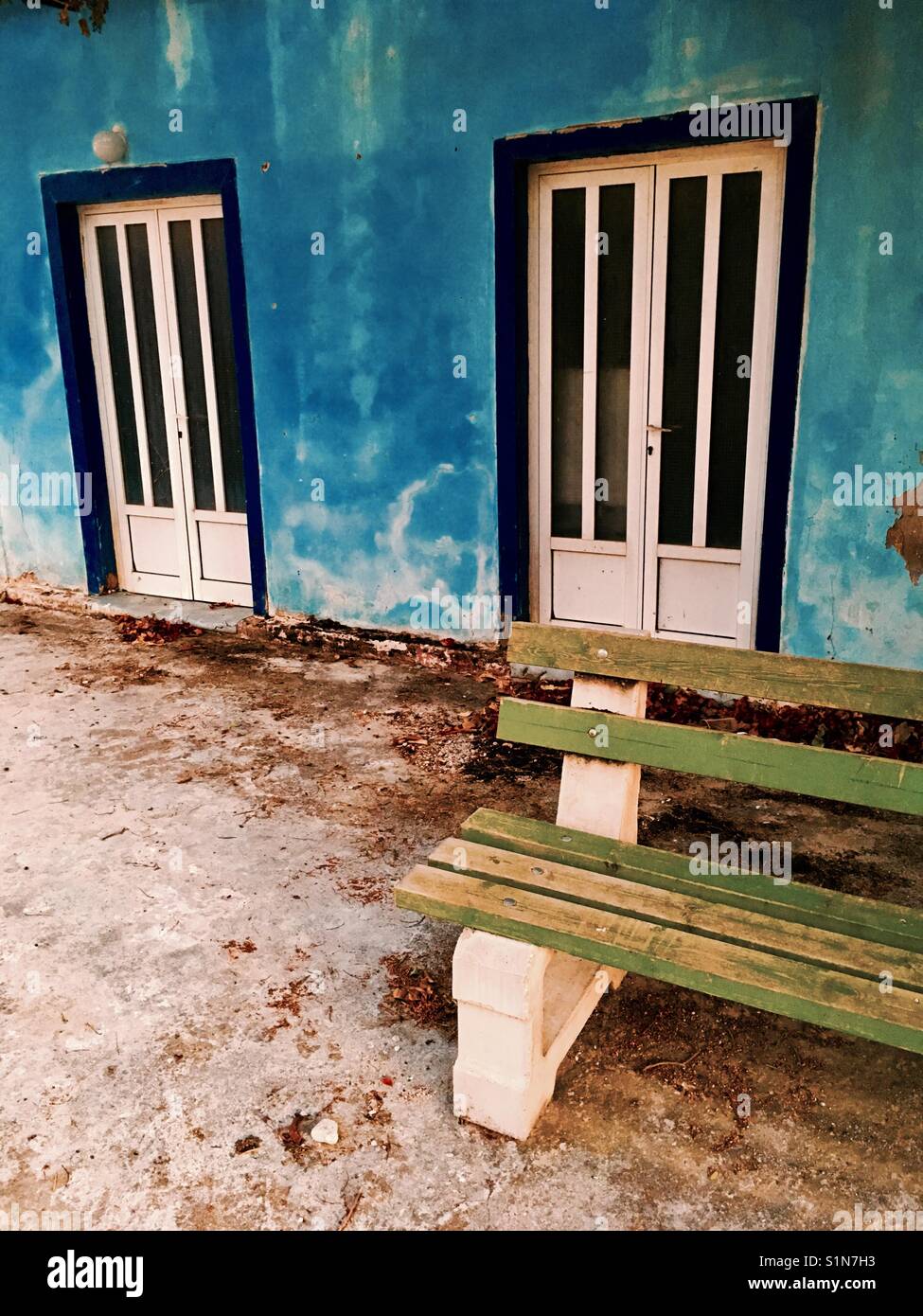 Green bench against blue house with two white doors in Svornata on Kefalonia island in Ionian Sea in Greece - Smartphone Captured Stock Image