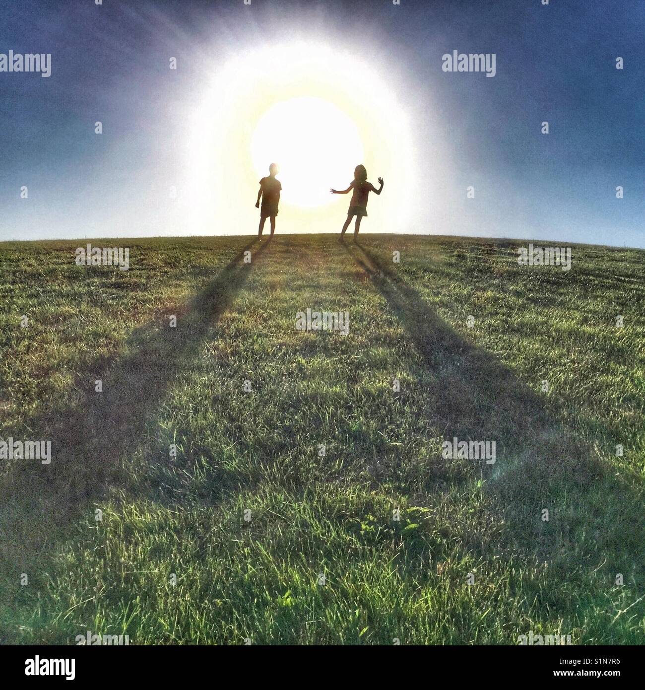 Two kids standing on top of a big hill with blazing sun behind them. - Smartphone Captured Stock Image