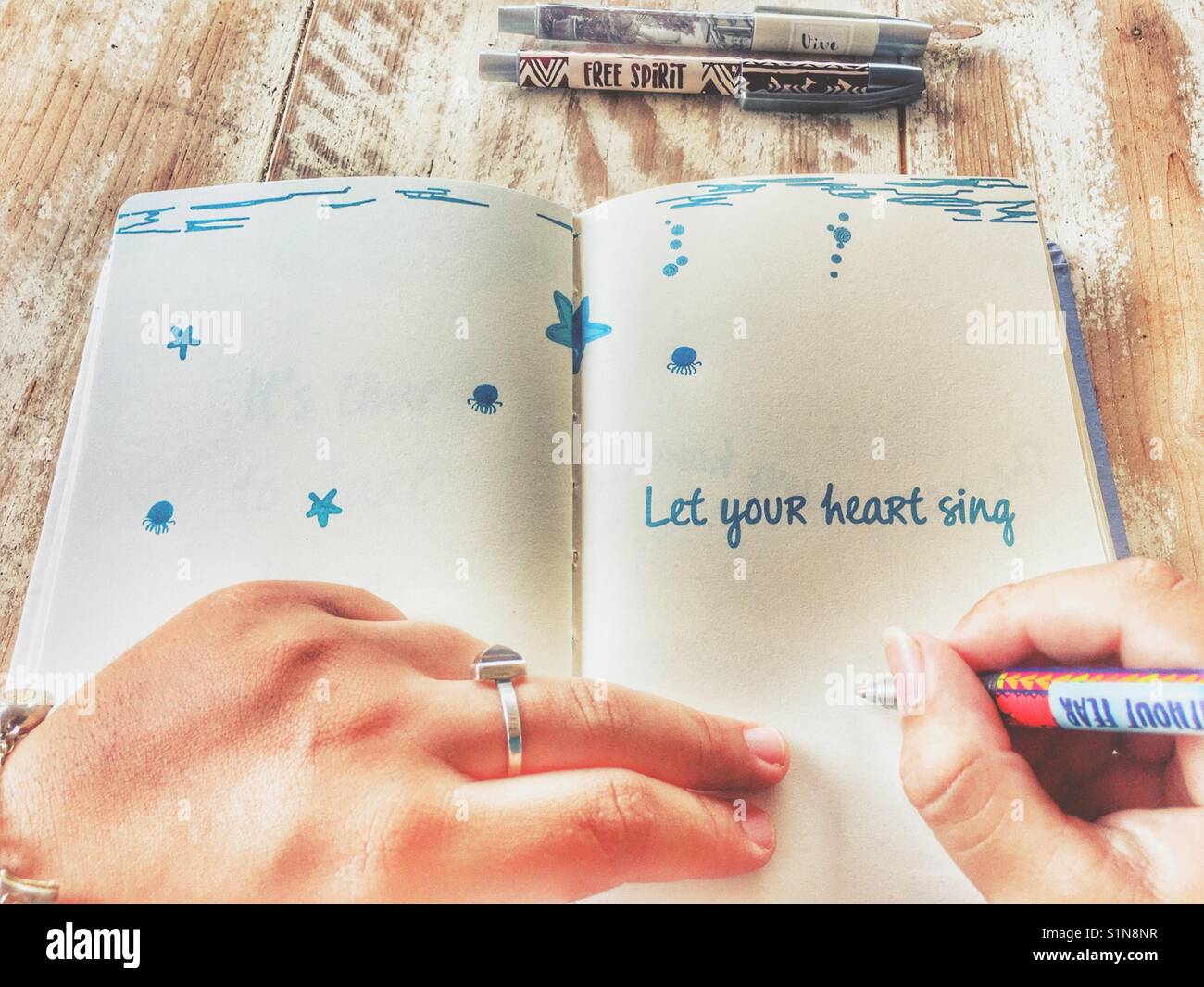 Woman writing in a journal open to a page with the mantra Let Your Heart Sing - Smartphone Captured Stock Image