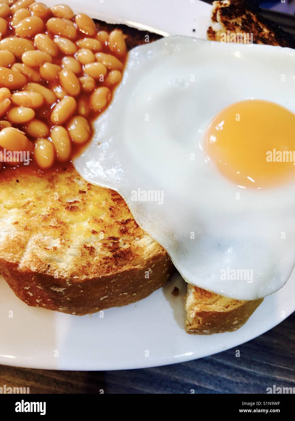 Baked beans on thick sliced toast with a fried egg Stock Photo