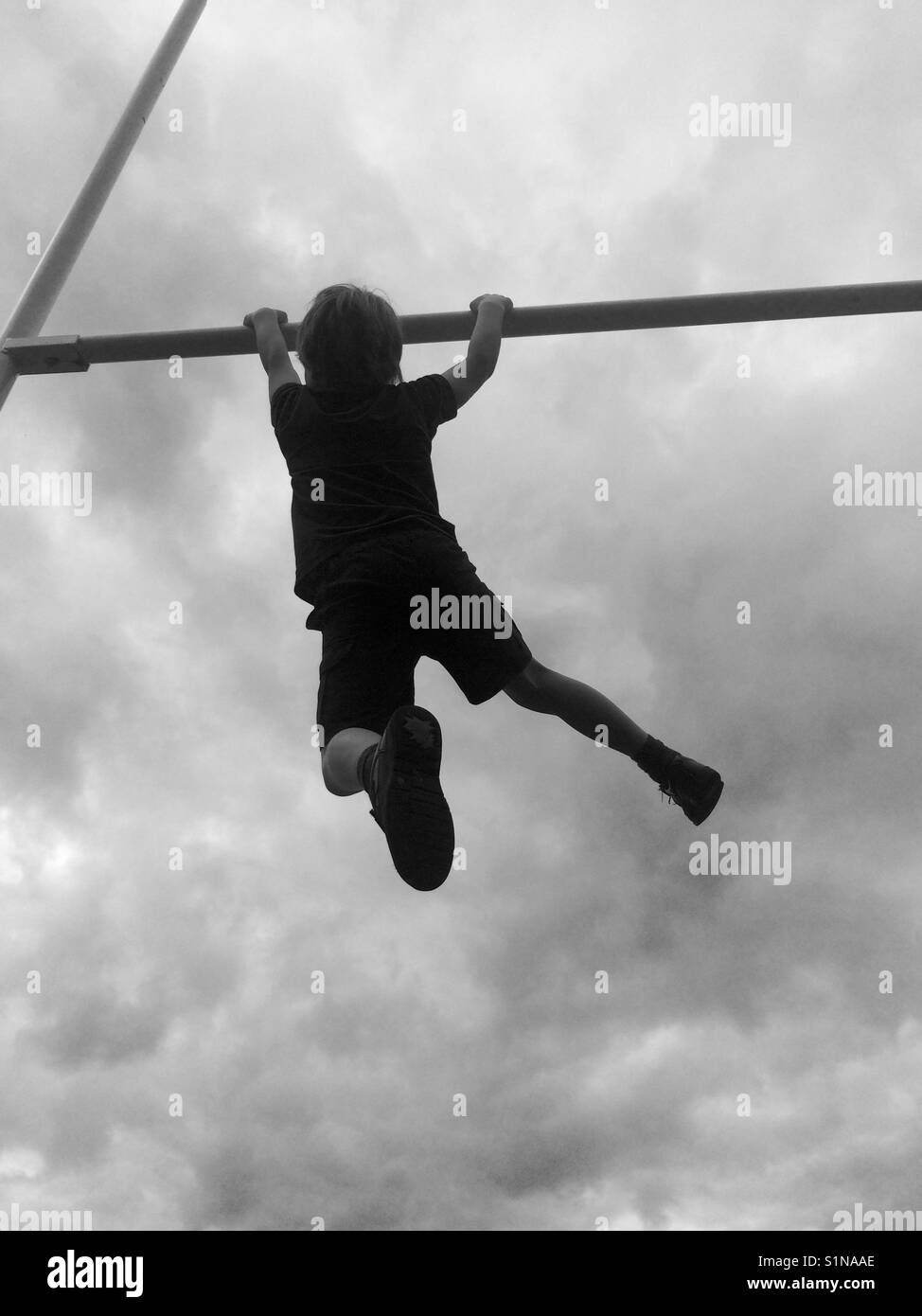 Boy hanging from a bar Stock Photo