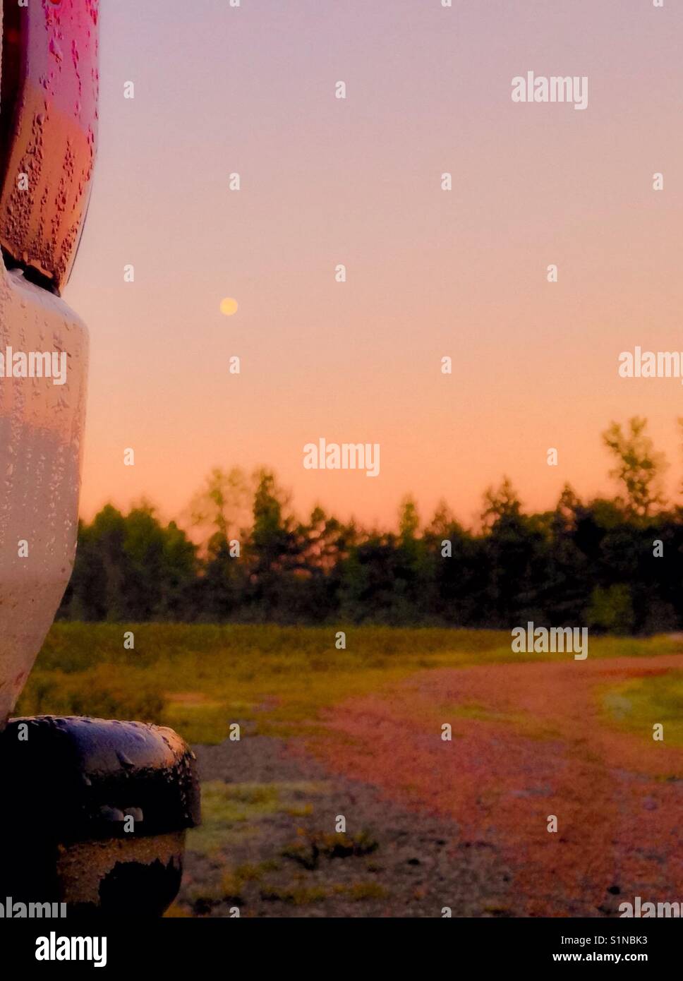 Full moon at dawn- full moon framed by pickup taillight and farm field at day break in North Carolina - Smartphone Captured Stock Image