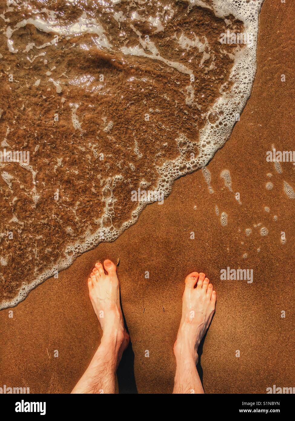 Man's feet in sand as tide comes in Stock Photo