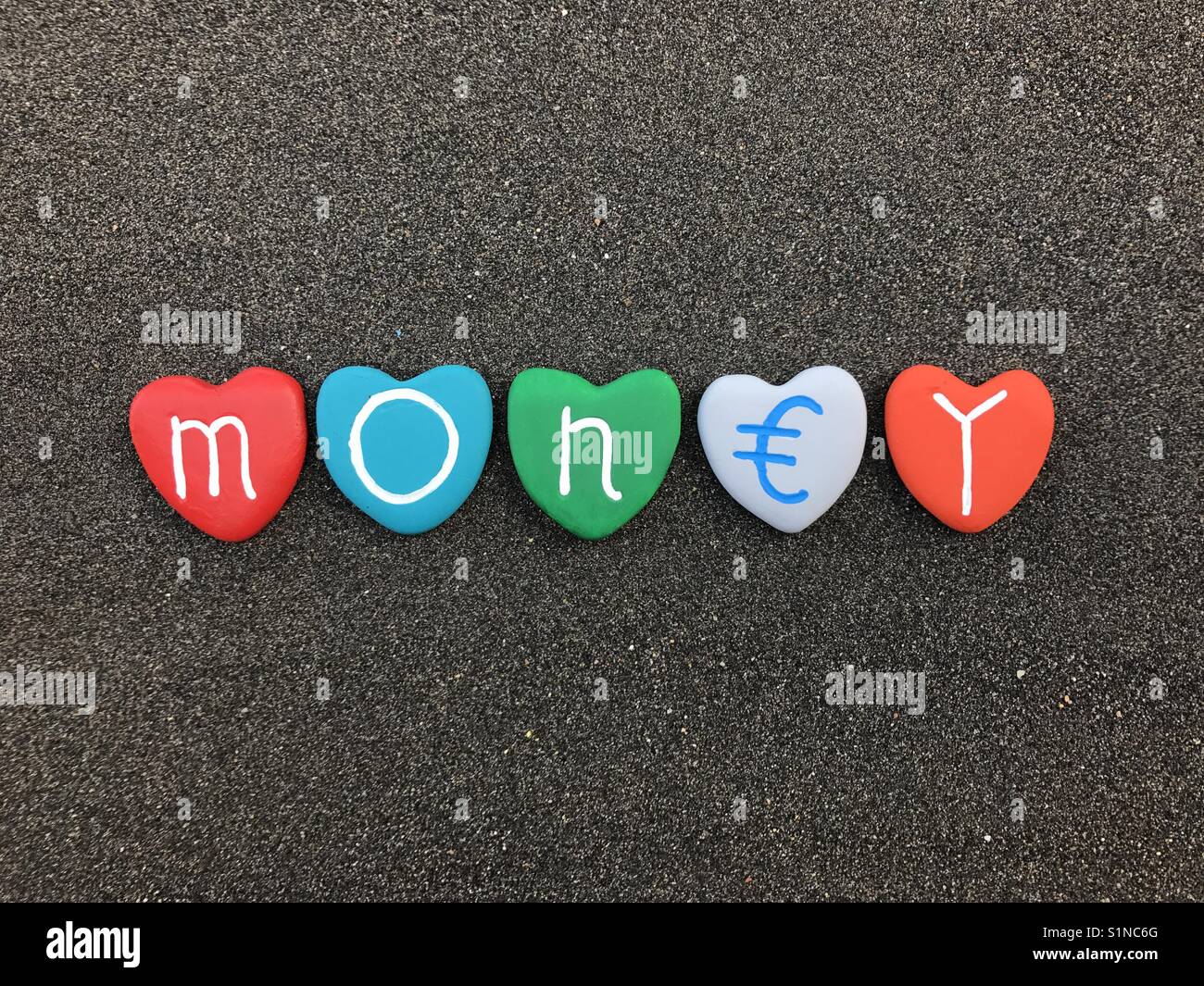 Money, conceptual artwork with colored heart stones over black volcanic sand Stock Photo