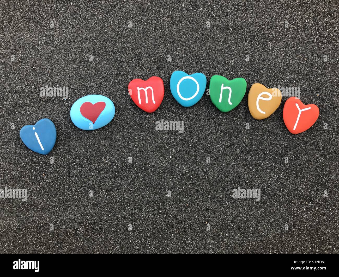 I love money concept with colored heart stones over black volcanic sand Stock Photo