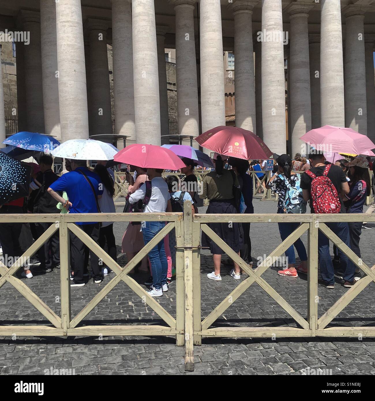 Asian tourists holding umbrellas to protect themselves from the sun, are queuing in St. peter's