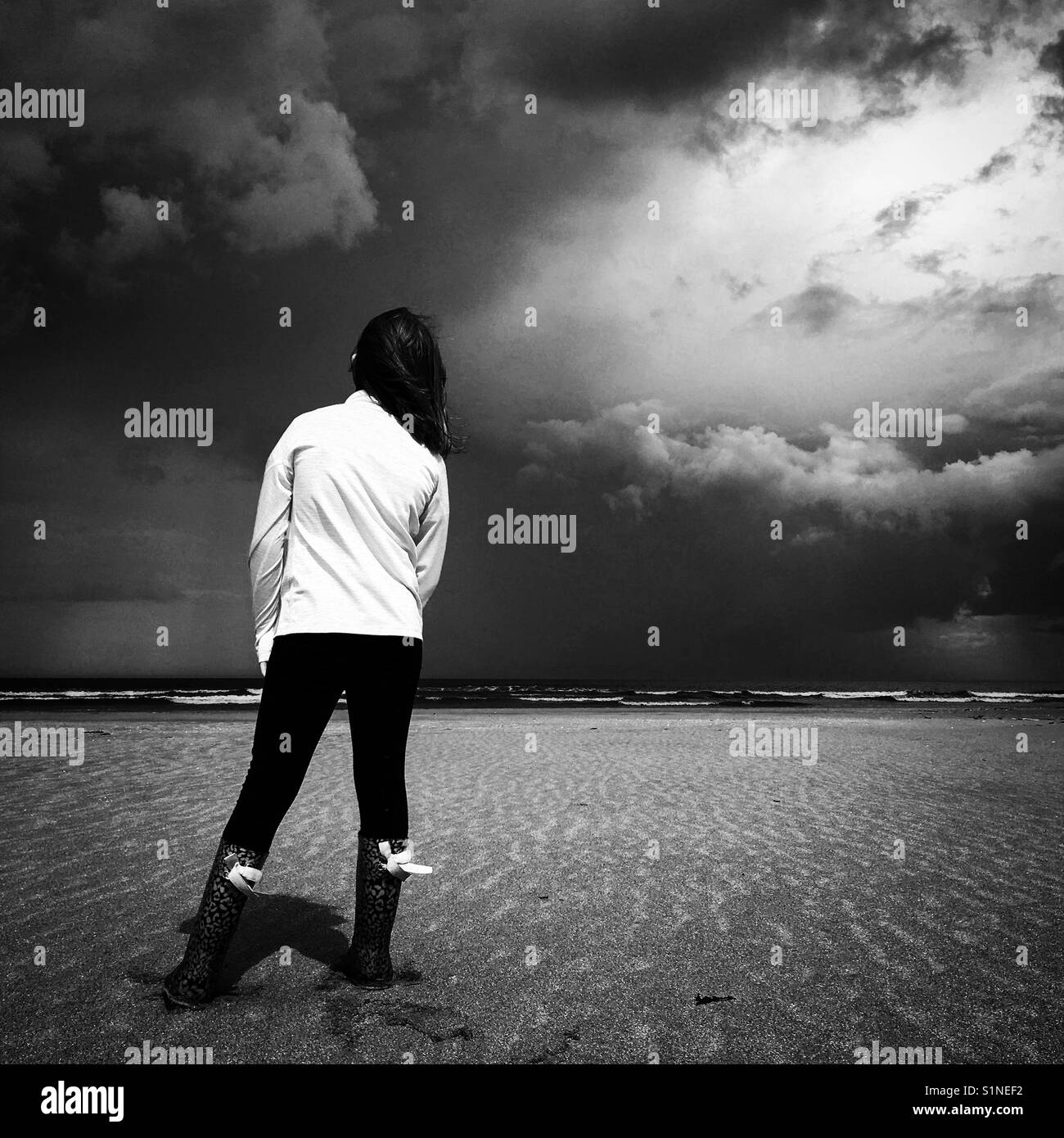 A girl stood watching the storm coming on an empty beach Stock Photo - Alamy