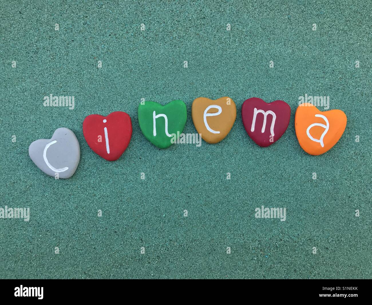 Cinema word with colored heart stones over green sand - Smartphone Captured Stock Image