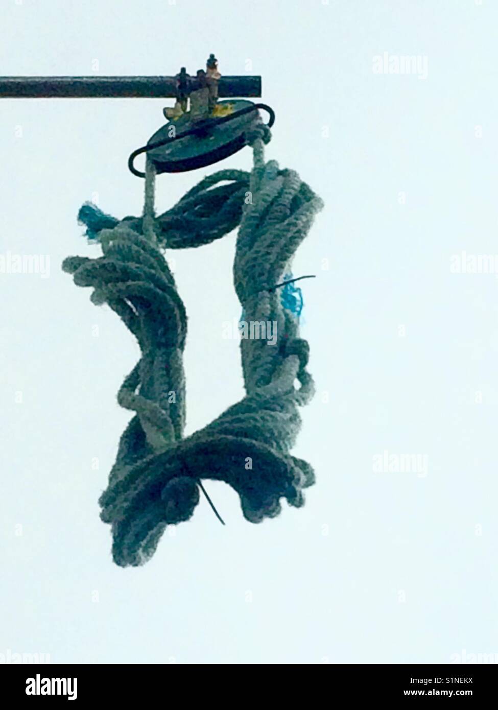 Rectangle of rope hanging from pulley against grey sky Stock Photo