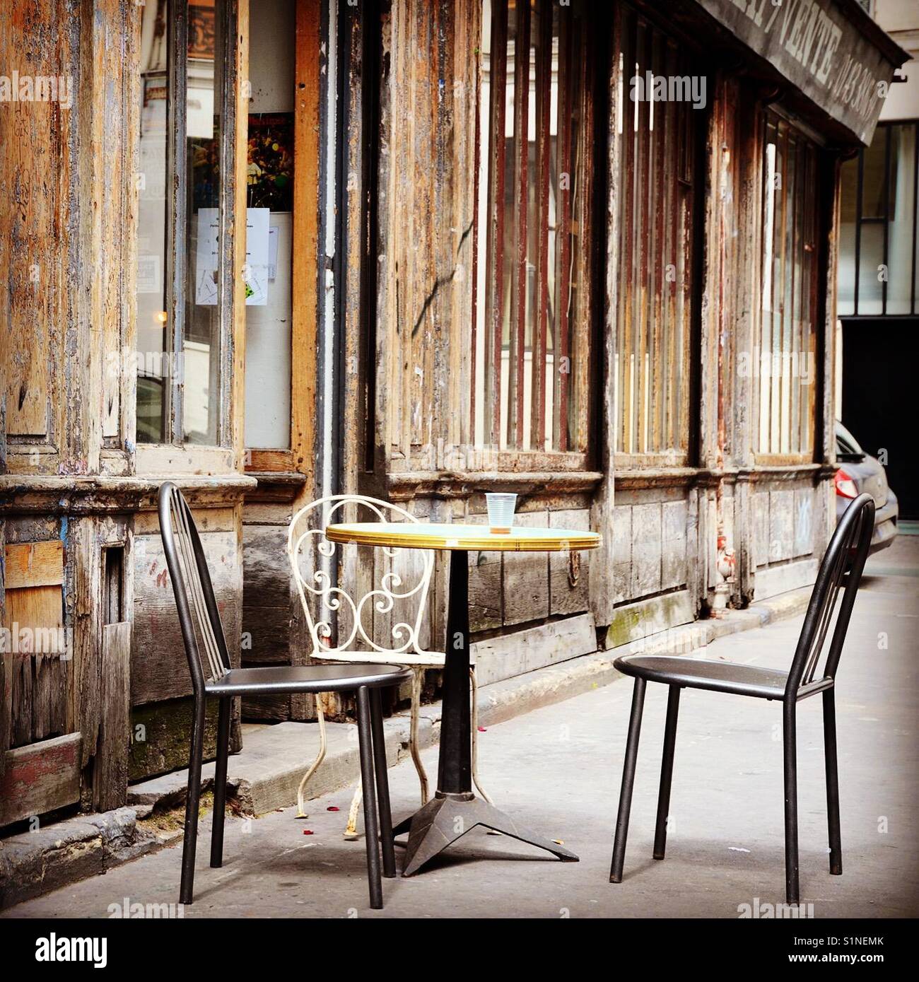 Three empty chairs and a table in a Parisian street in front of a shop - Smartphone Captured Stock Image