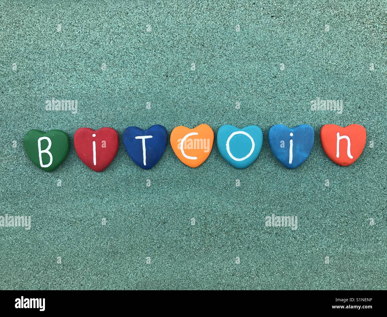 Bitcoin, worldwide cryptocurrency and digital payment system with colored heart stones over green sand - Smartphone Captured Stock Image
