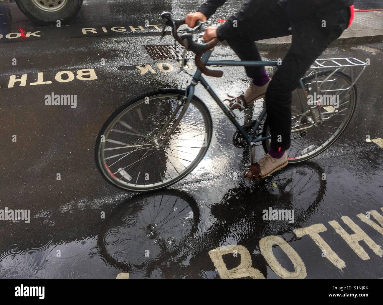 A man cycles through the rain in London, England - Smartphone Captured Stock Image