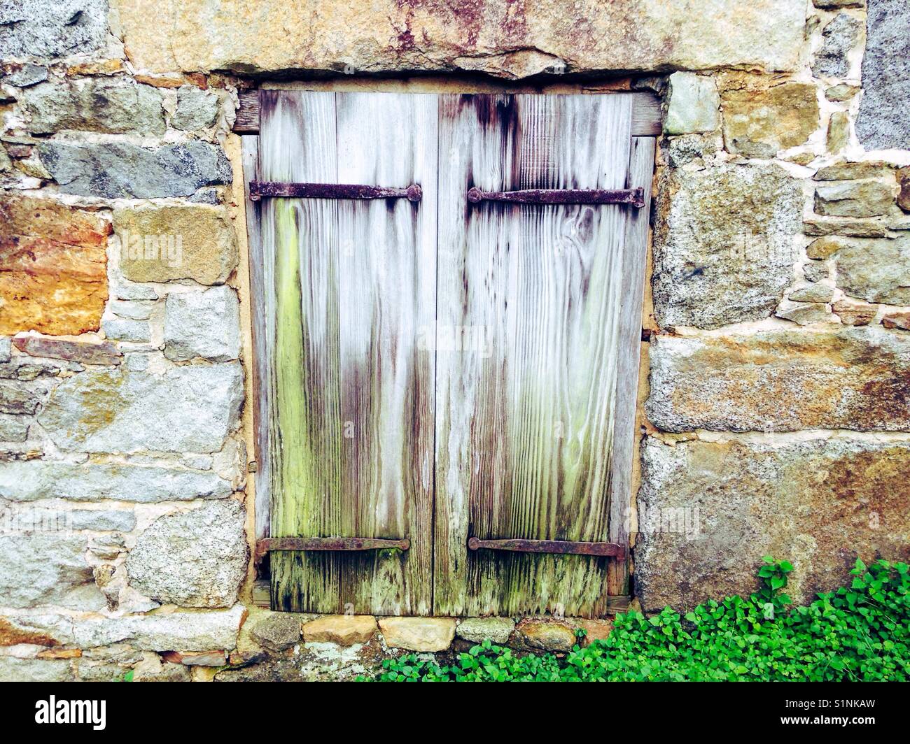 Ground level wooden window shutters with wrought iron hinges - Smartphone Captured Stock Image