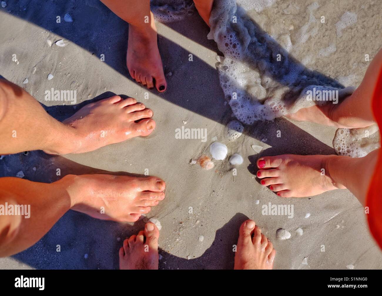 4 pair of feet in circle on beach with wave Stock Photo