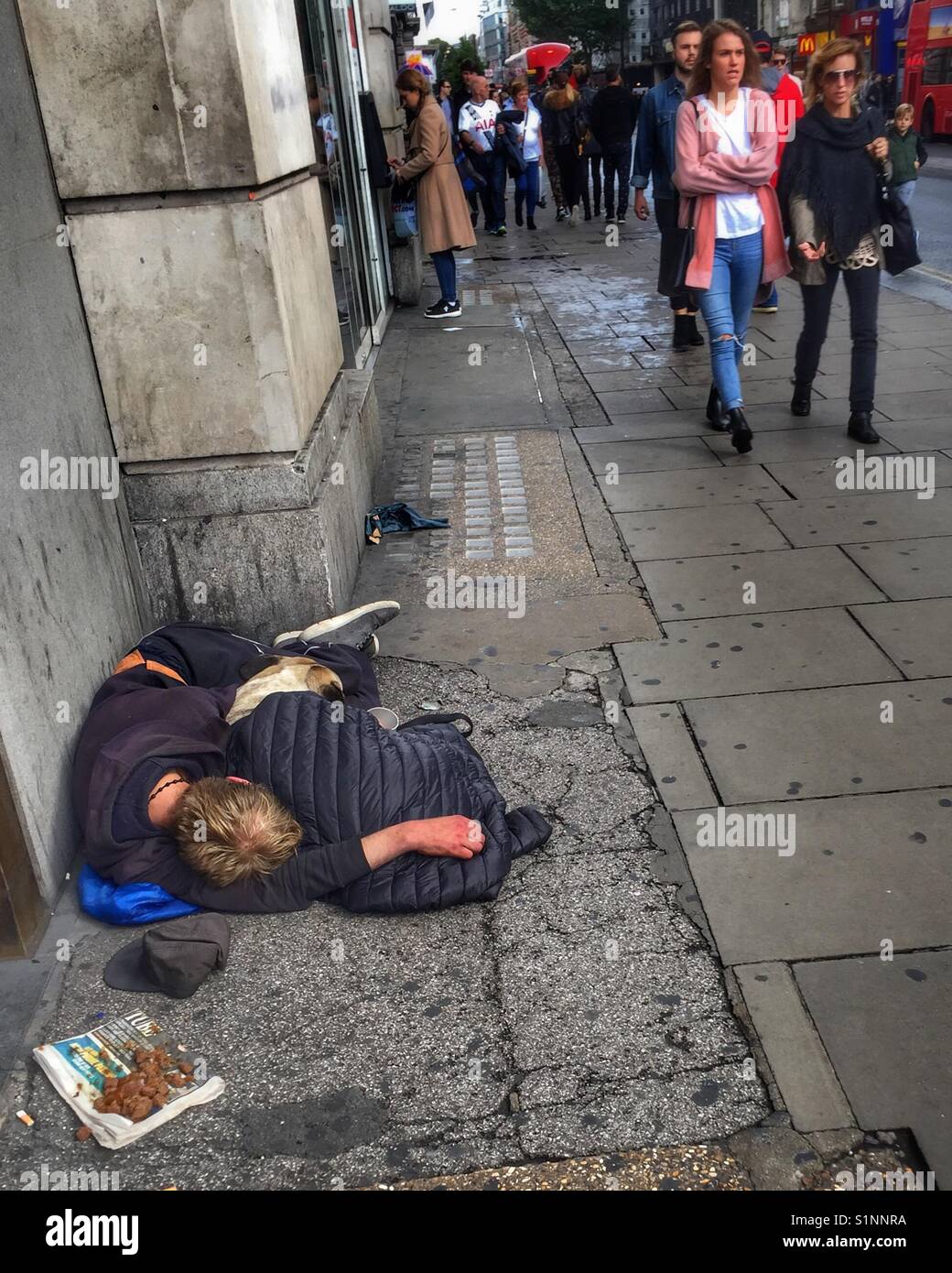 A homeless man sleeps with his dog outside a shop on Tottenham Court Road in London, England Stock Photo