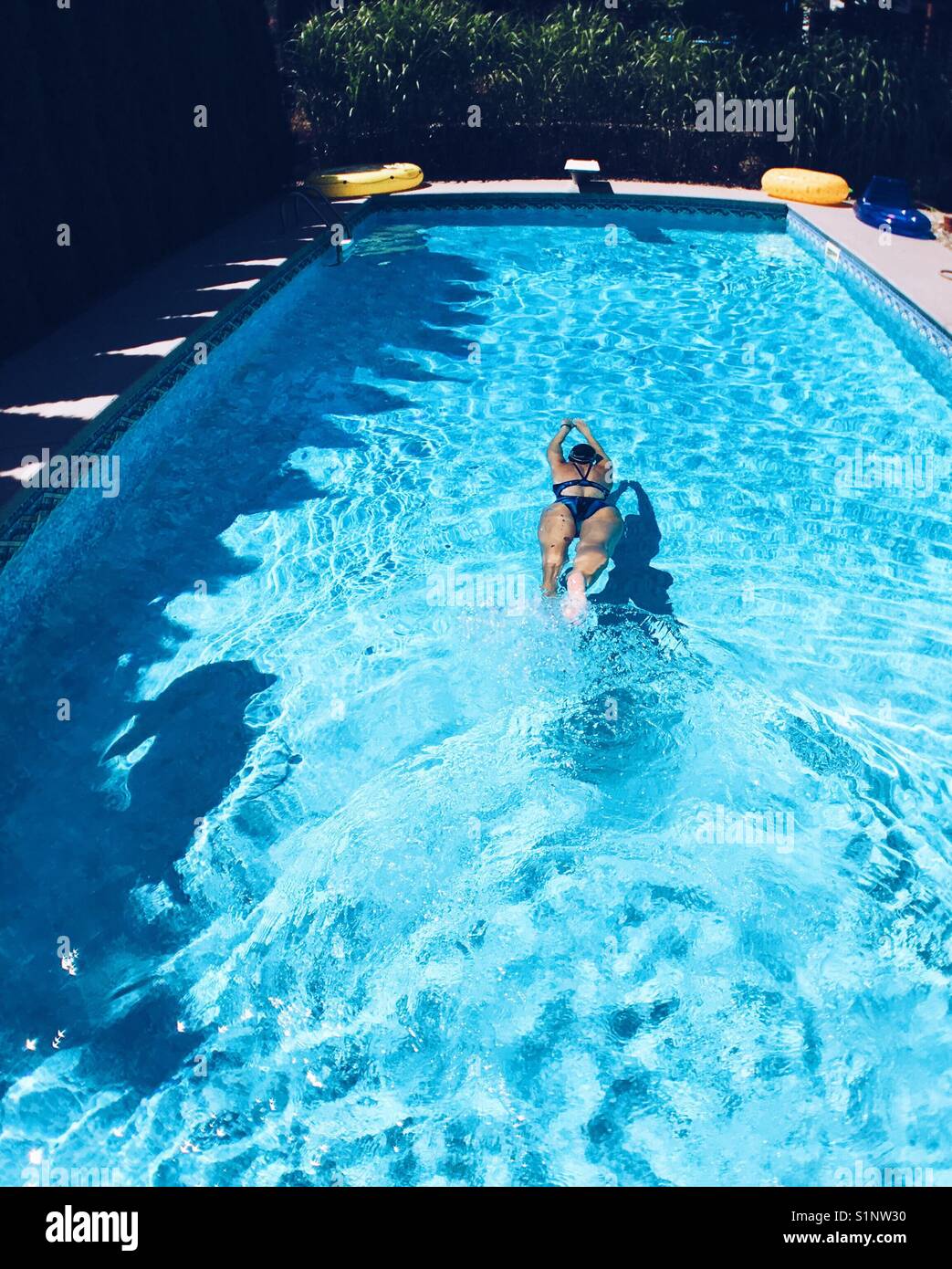 Woman swimming in a pool on a sunny day outdoors. - Smartphone Captured Stock Image