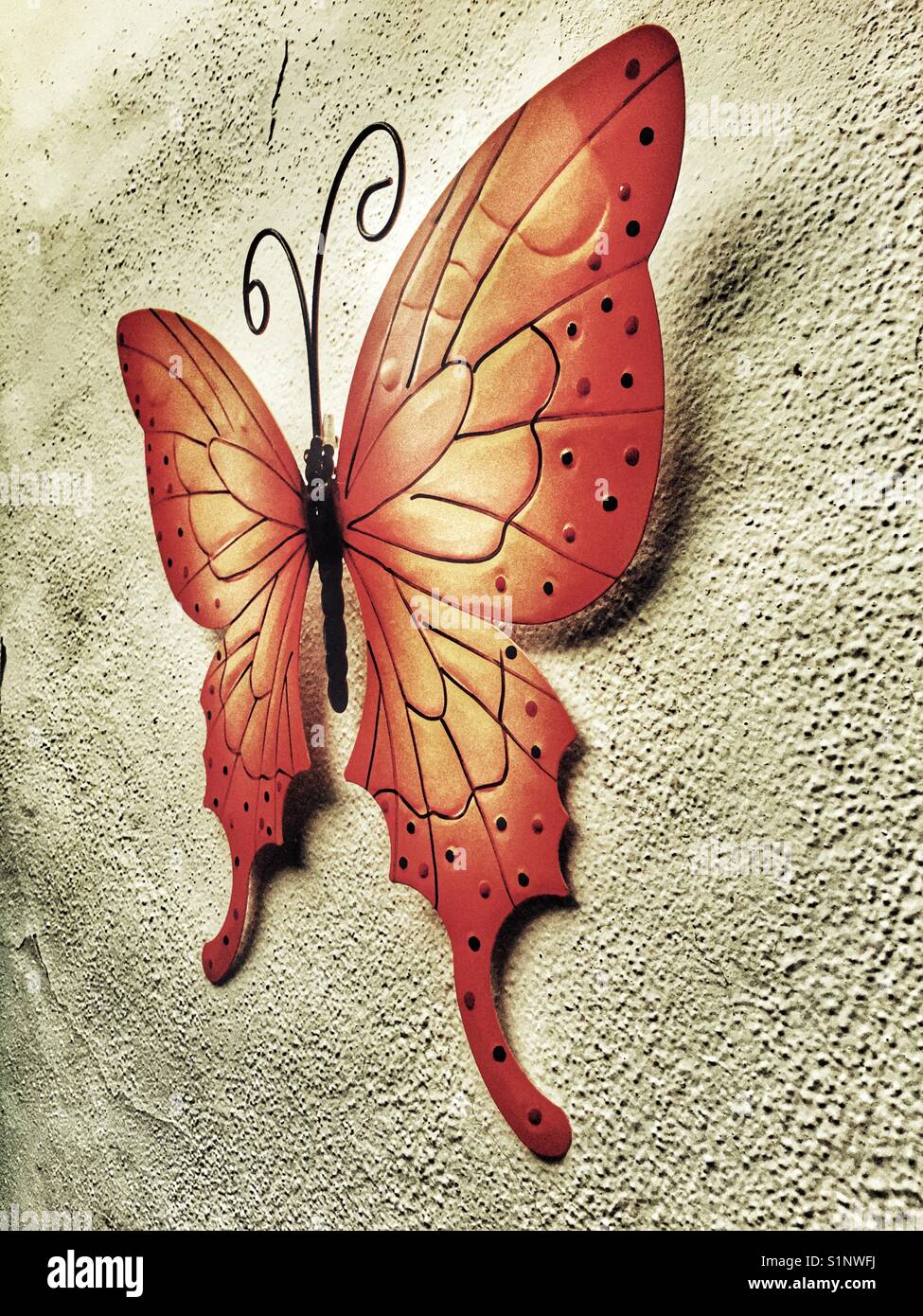 Metal butterfly, painted orange, on a wall - Smartphone Captured Stock Image