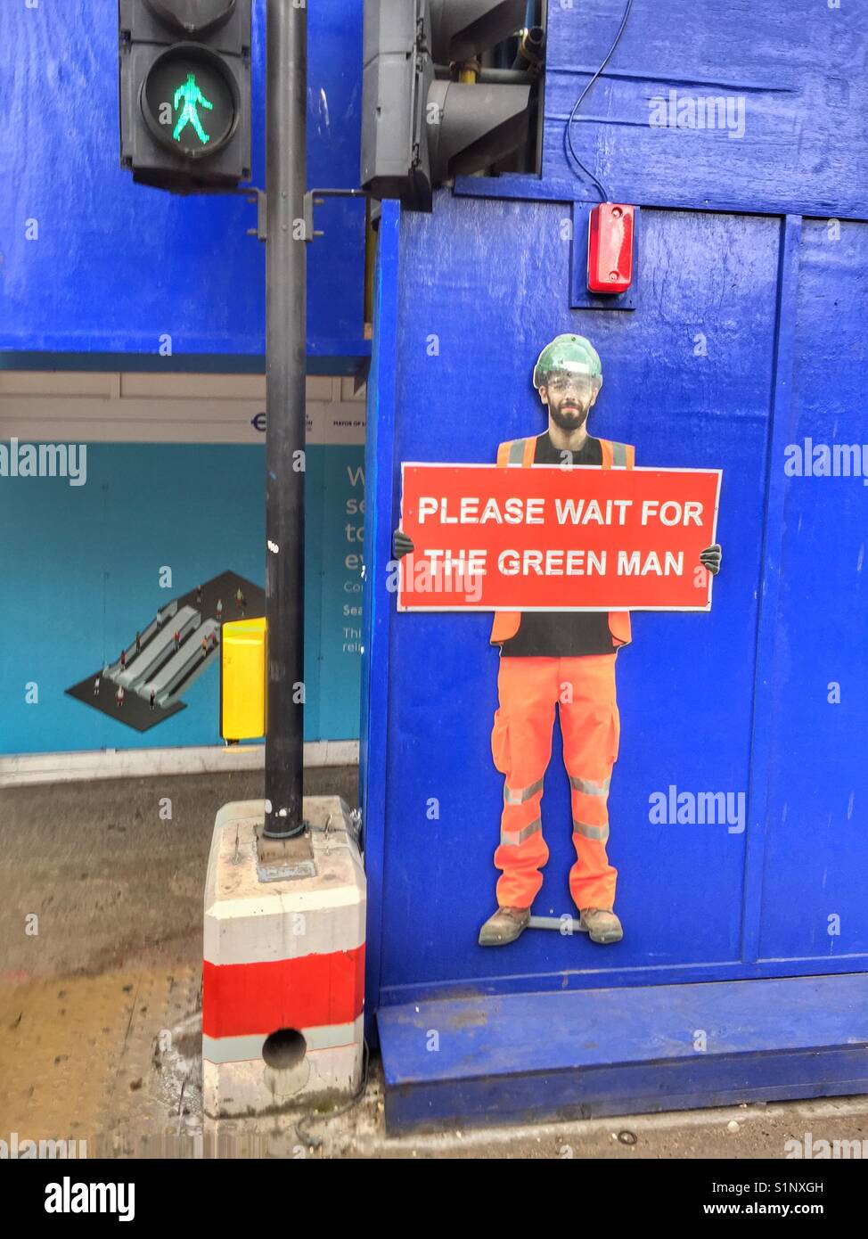 A cut out of a man holding a sign which says 'please wait for the green