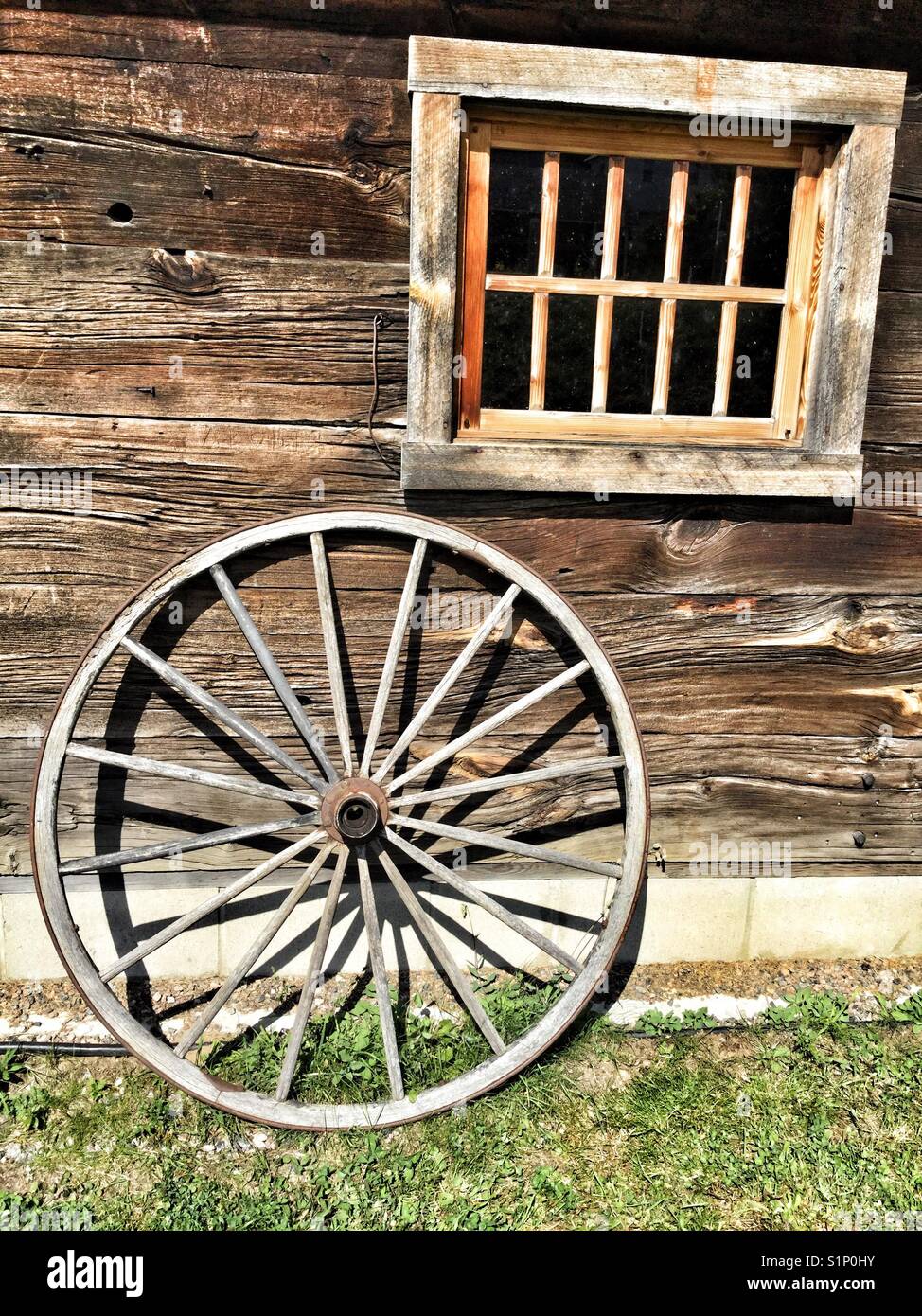 Wooden wagon wheel leaning against a log house. Stock Photo