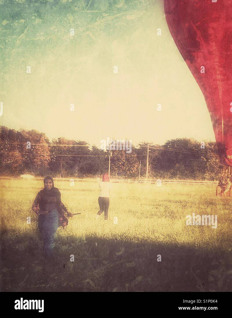 A young lady runs after exiting a hot air balloon, while her friend takes photos.  Grunge effect added. - Smartphone Captured Stock Image