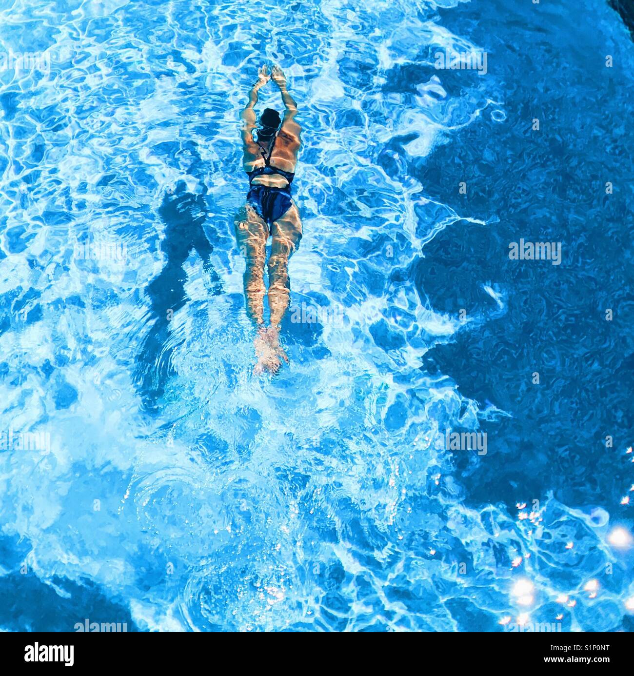 Woman swimming face down in outdoor swimming pool on a sunny day. Stock Photo