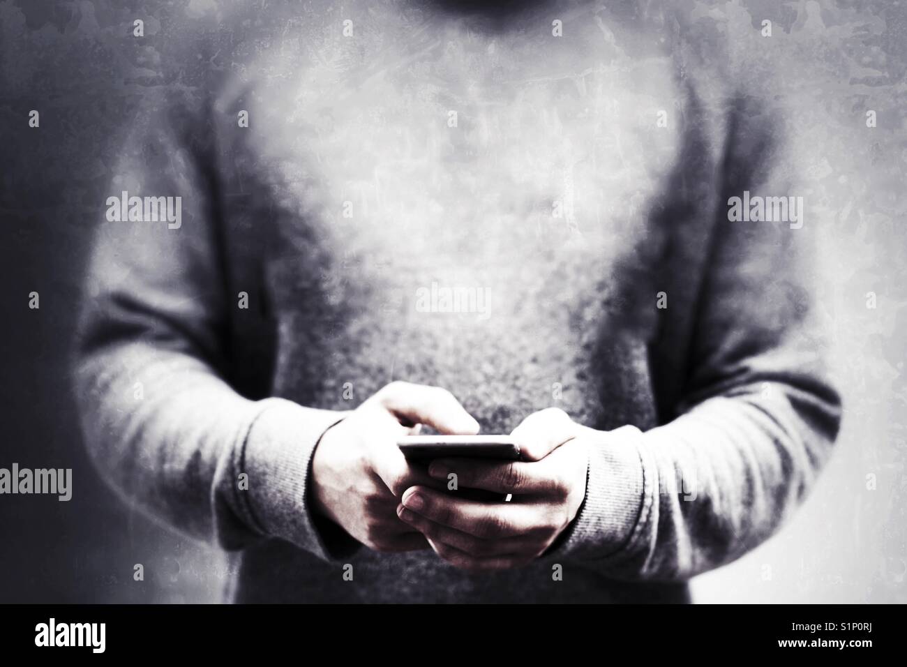 A male hipster in metallic silver sweatshirts holding up his mobile phone whilst texting in a dark, devious mid section image - Smartphone Captured Stock Image