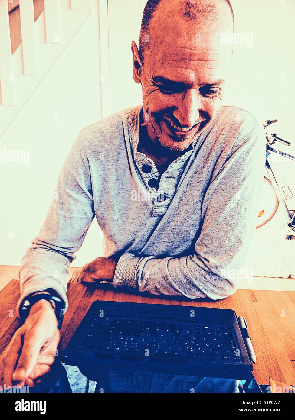 Smiling middle aged Scandinavian man working on laptop at home - Smartphone Captured Stock Image
