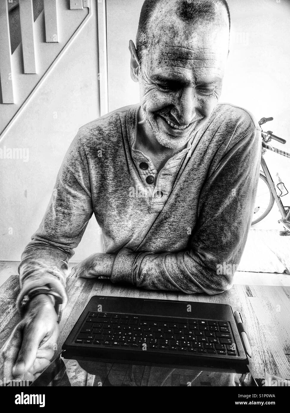 Smiling middle aged Scandinavian man working on laptop at home - Smartphone Captured Stock Image