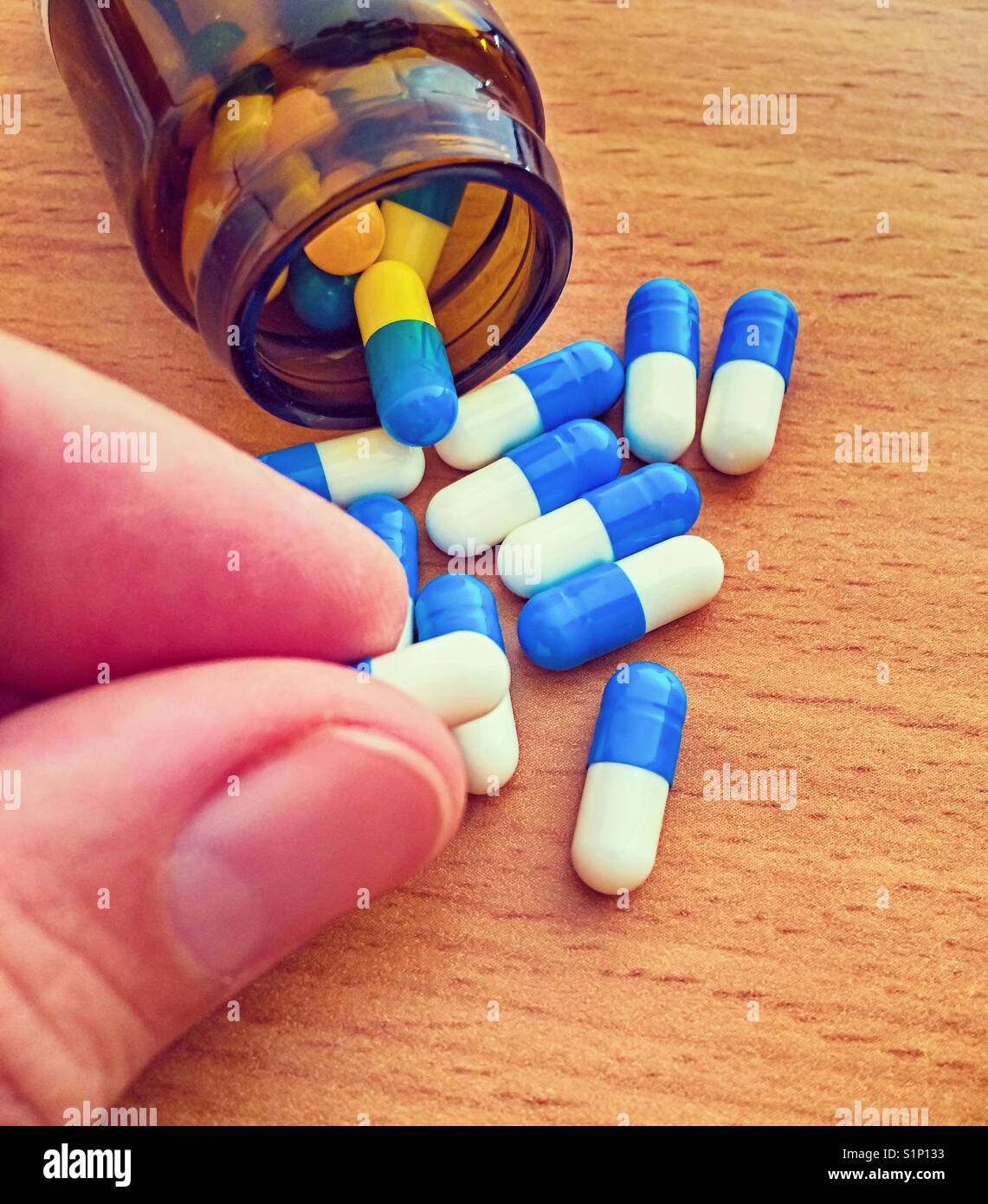 Woman fingers taking pill from heap of pills spilling out from bottle Stock Photo