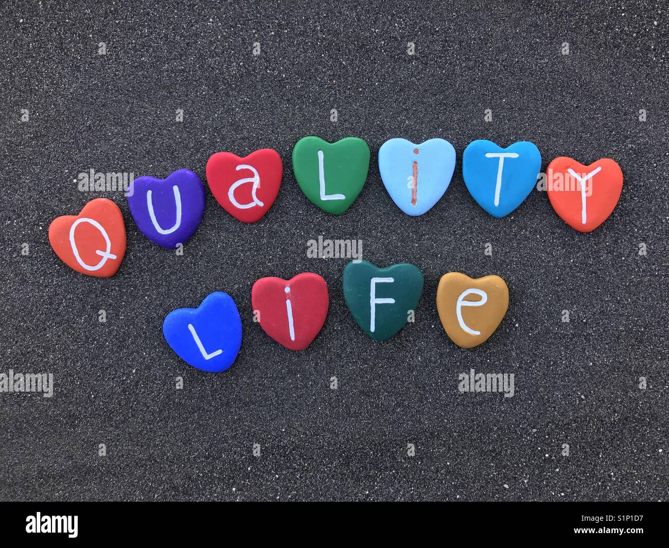Quality life, better future, colored heart stones composition over black volcanic sand Stock Photo