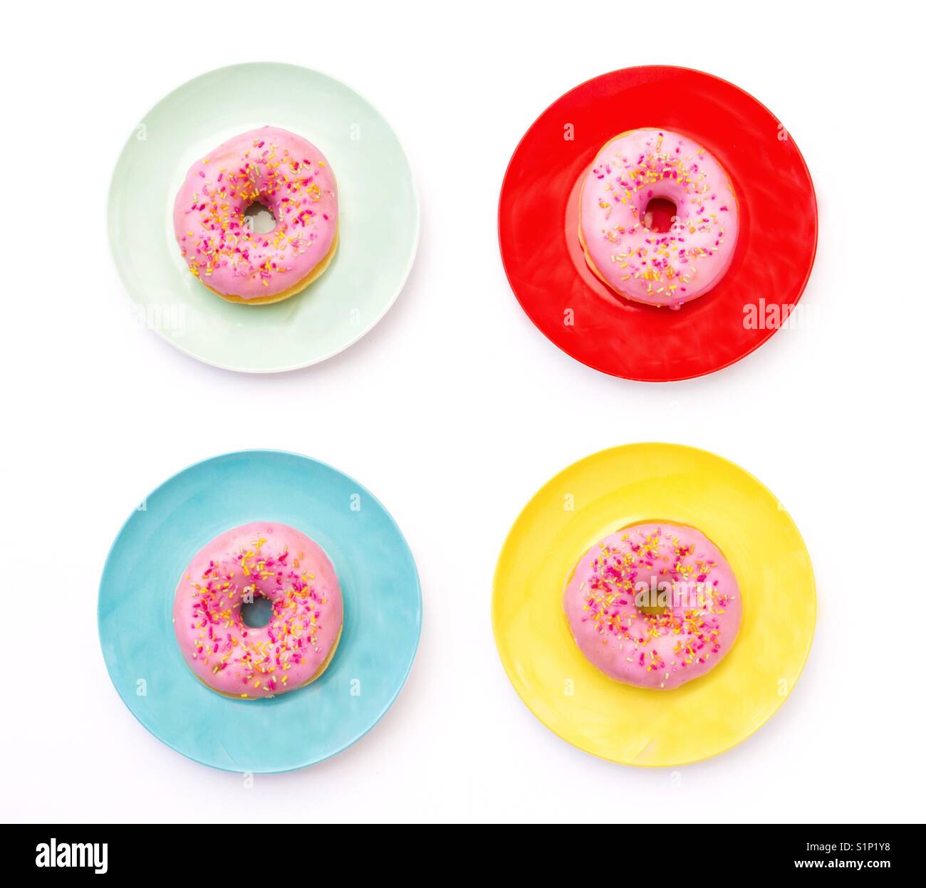 Looking down from above onto for colourful plates with donuts sitting on them that have pink icing with hundreds and thousands - Smartphone Captured Stock Image