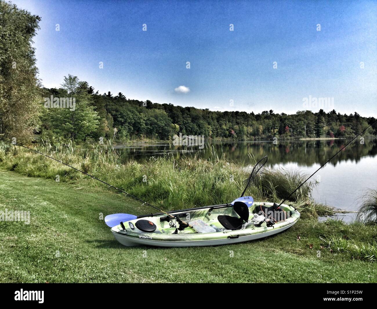 A fishing kayak on the grass next to a calm lake. - Smartphone Captured Stock Image