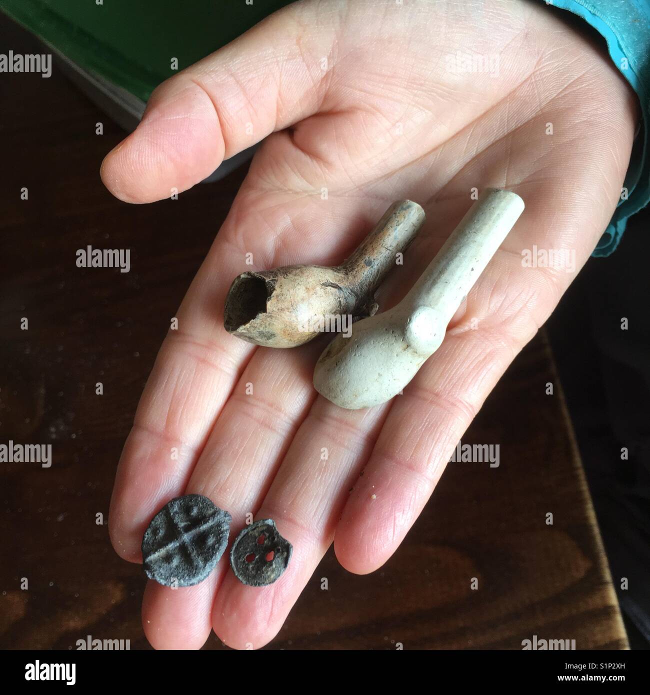 Woman's hand displaying Mudlarking finds of medieval traders token and old clay pipes Stock Photo