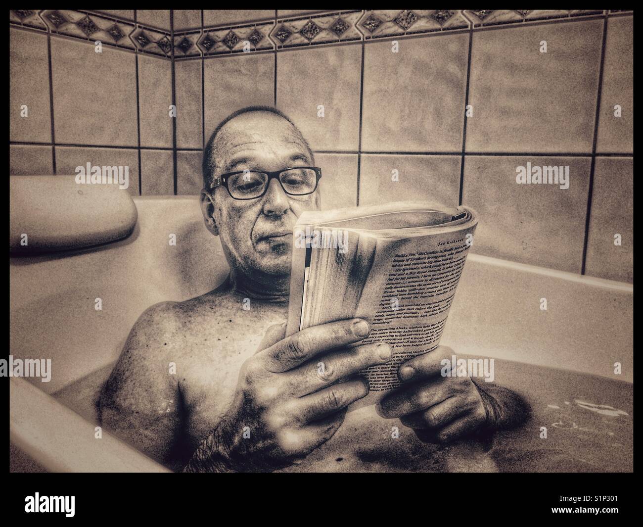 Middle aged man in glasses reading a book in the bath - Smartphone Captured Stock Image