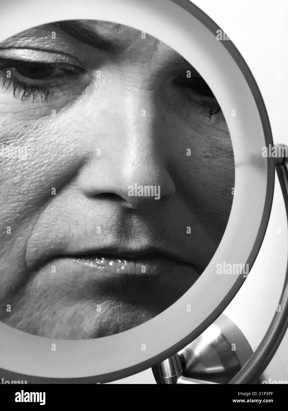 A black and white closeup of a woman's face in a make up magnifying mirror - Smartphone Captured Stock Image