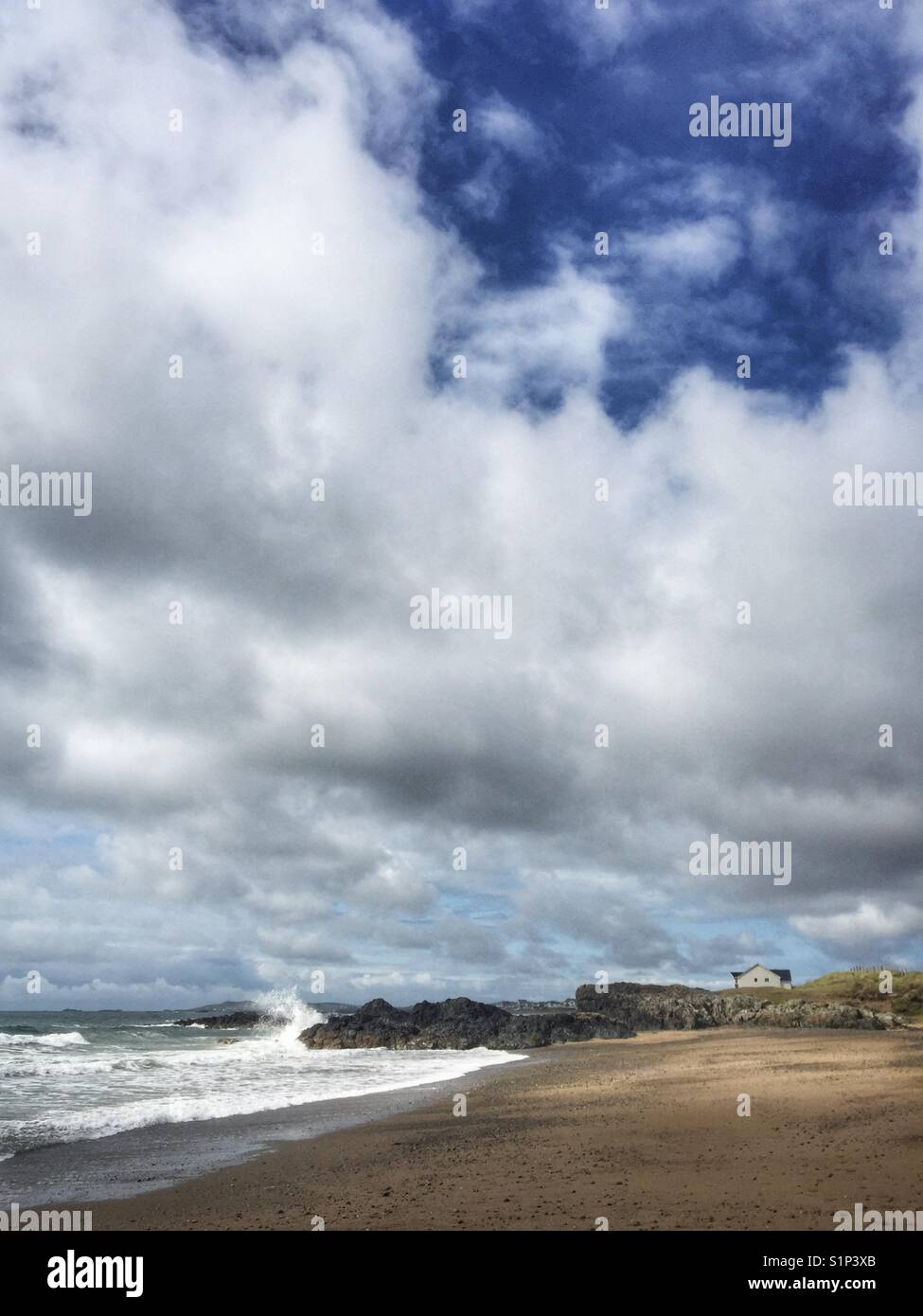 Lone house on beach with waves crashing against rocks, Rhosneigr, Anglesey, North Wales - Smartphone Captured Stock Image