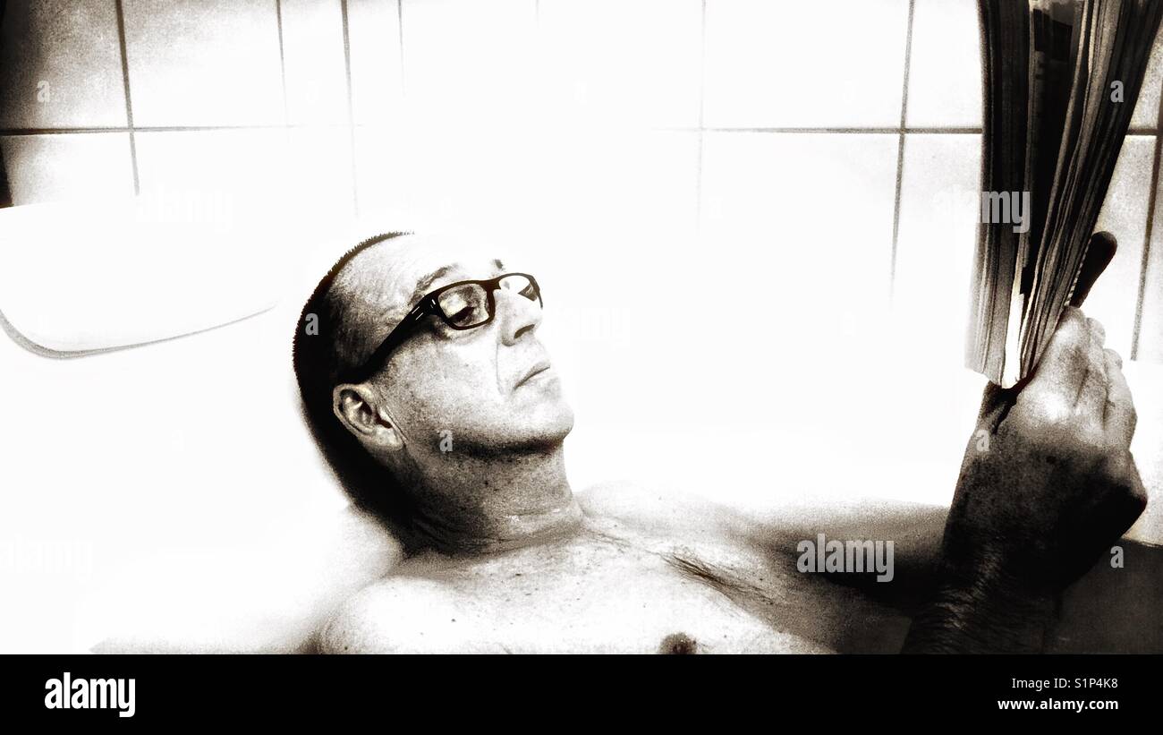 Middle aged man relaxing reading a book in the bath - Smartphone Captured Stock Image