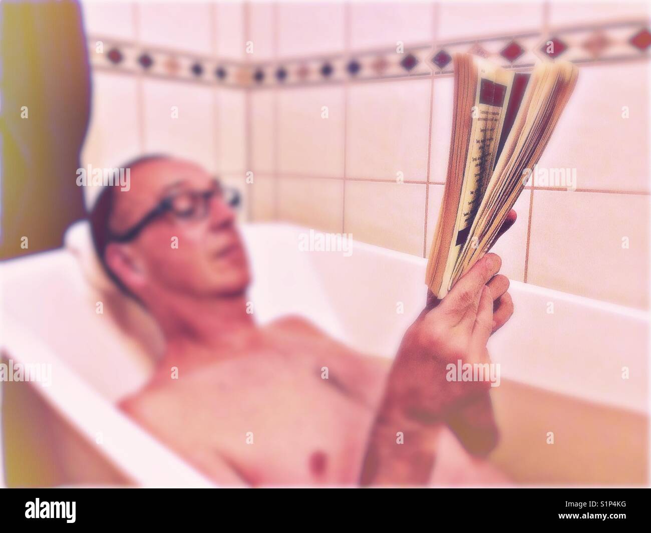 Middle aged man relaxing reading in bath blur with focus on book Stock Photo
