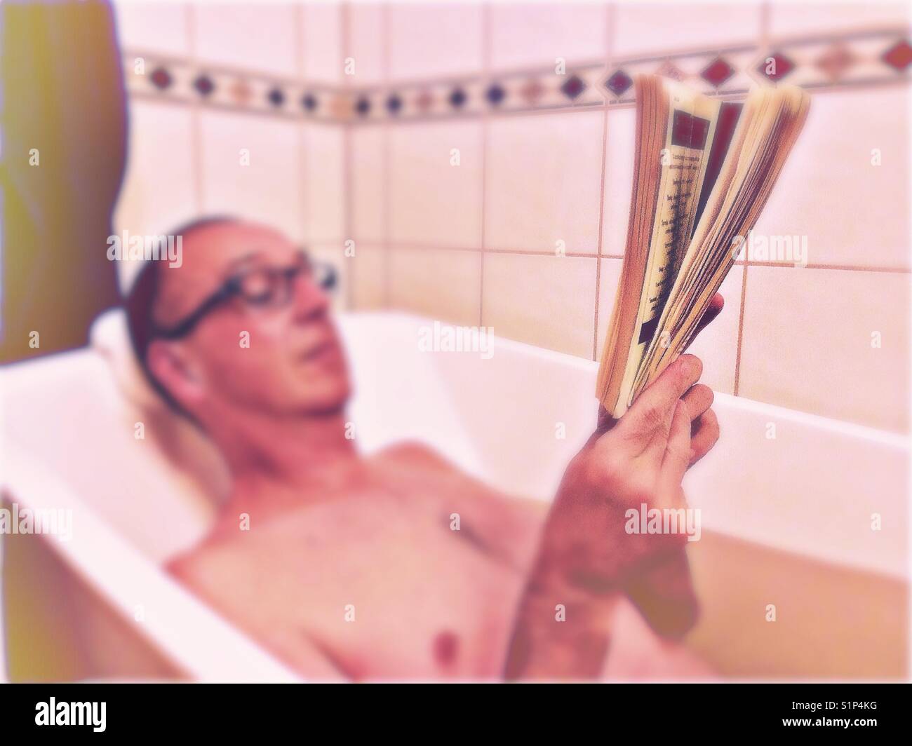 Middle aged man relaxing reading in bath blur with focus on book - Smartphone Captured Stock Image