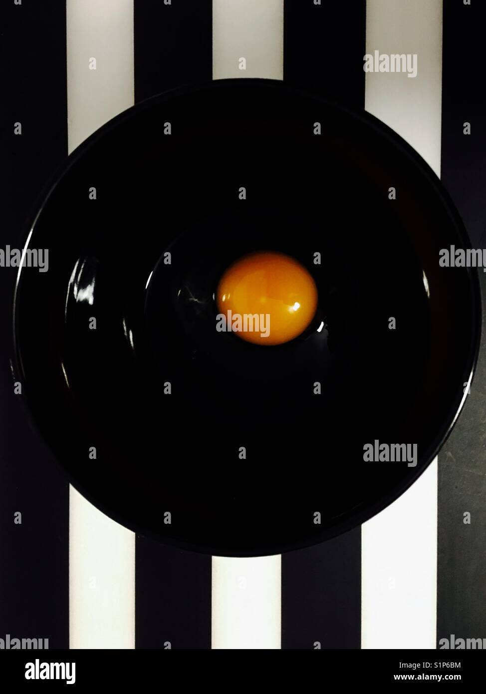Egg yolk in a black bowl against black and white stripes - Smartphone Captured Stock Image