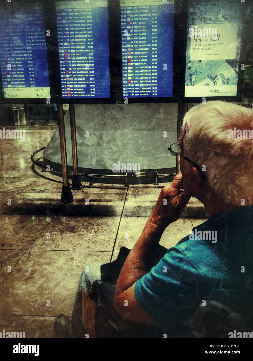 Senior man in a wheelchair, looking at the departure board at night, flight delayed. El Altet airport, Alicante, Spain Stock Photo